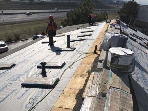 Two roofing repair workers in construction gear stand on an exposed roof