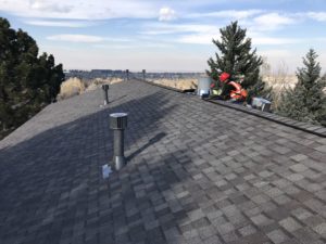 Two roofers wearing red construction hats repair a gray roof in Denver