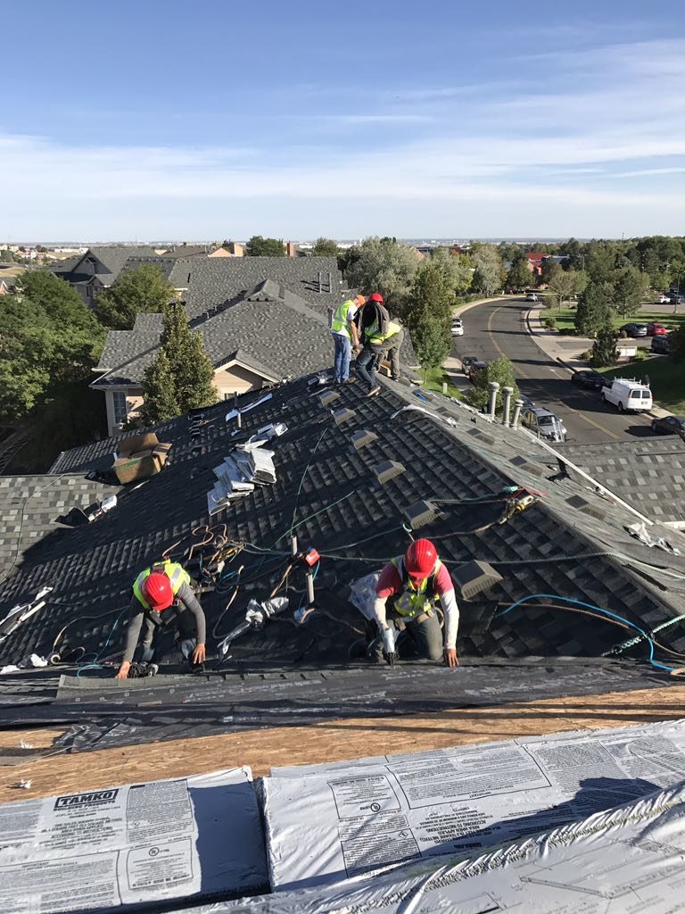 Several roofers work on replacing a roof under blue skies in Colorado